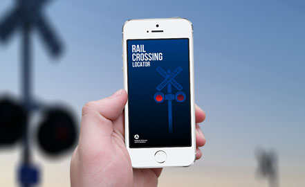 Primer plano del teléfono inteligente que muestra el localizador de cruces ferroviarios. El fondo es una imagen borrosa de un cruce de ferrocarril.